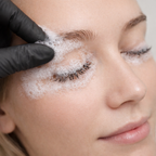 Close-up of a woman's face with a hand applying lash shampoo to her eyelashes.